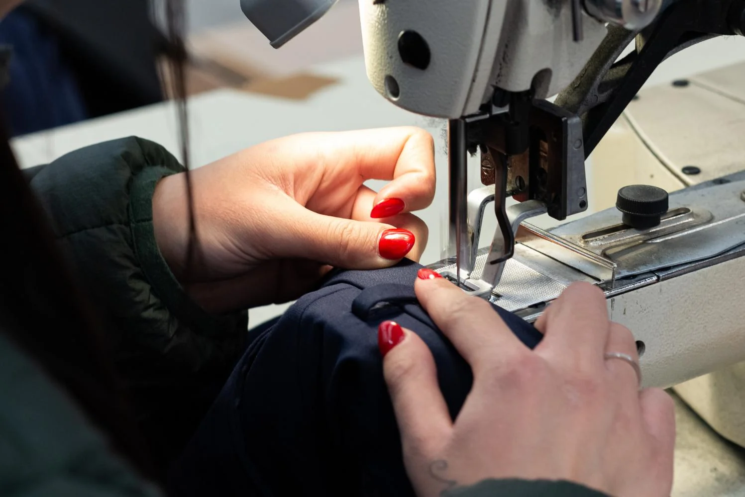 Le mani guidano un pantalone blu sotto l’ago della macchina da cucire