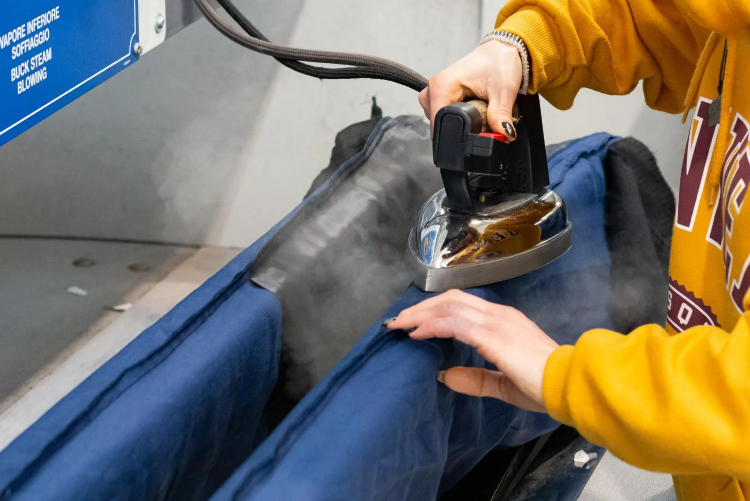 Una mano accompagna il ferro sul pantalone blu